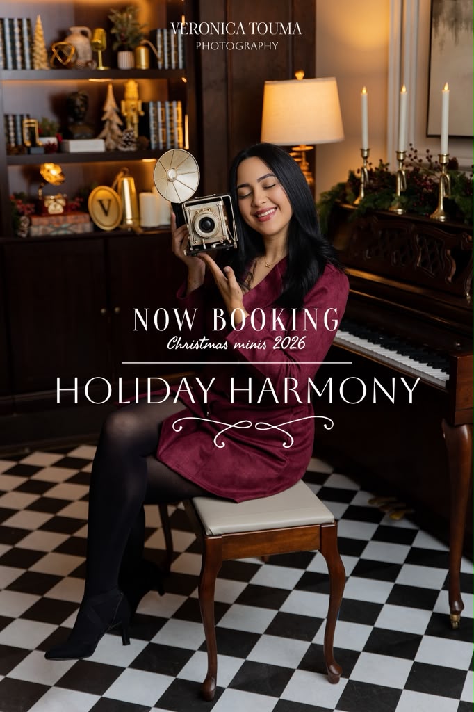 Now booking Christmas minis 2026: Holiday Harmony. Veronica in a burgundy dress holding a vintage camera beside a piano.