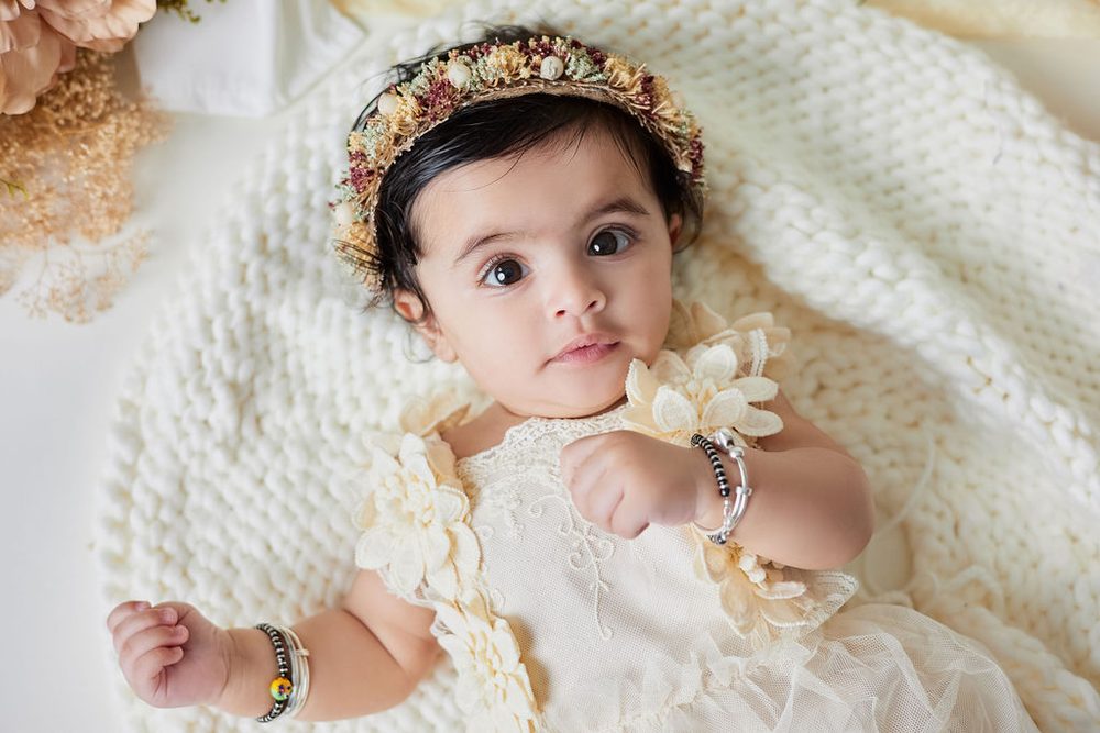 Baby in a flower crown and beaded bracelets lying on a knit blanket with a fist to her chest