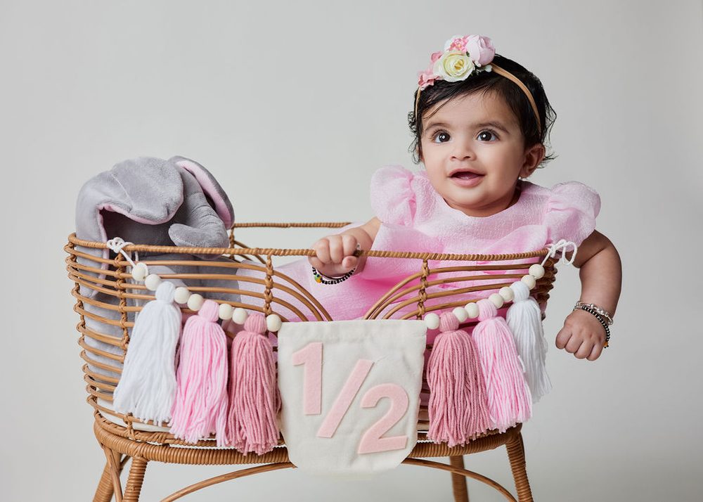 Baby in a pink tulle dress and rose headband peeking over a rattan basket with a felt '1/2' pennant