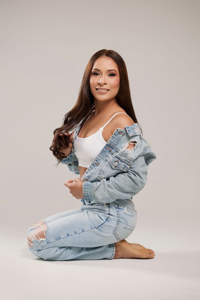 Smiling woman kneeling on the studio floor in jeans and a denim jacket slipping off one shoulder