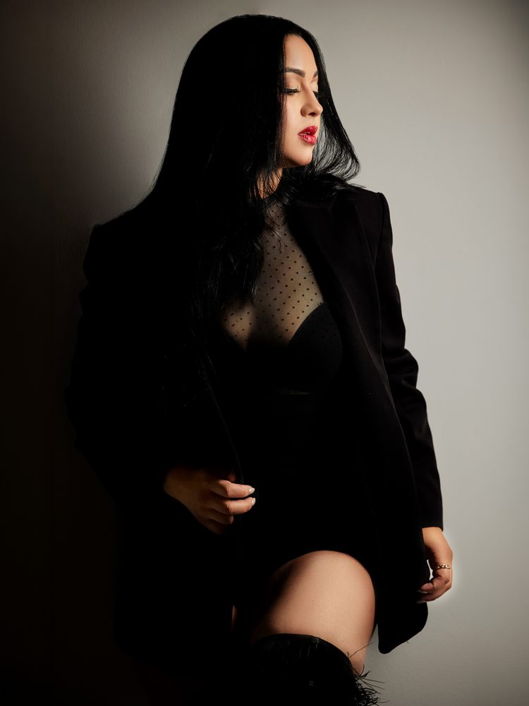 Close side-lit portrait of a woman with red lips and long black hair in a sheer dotted top and black blazer