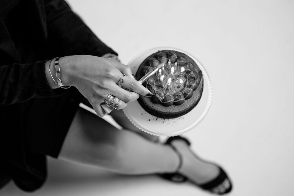 Black-and-white overhead close-up of ringed hands lighting candles on a chocolate cake with a long lighter
