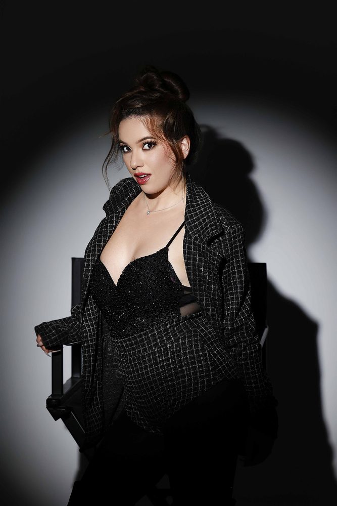 Spotlit woman with an updo and red lips glancing at the camera from a director's chair in a checked jacket