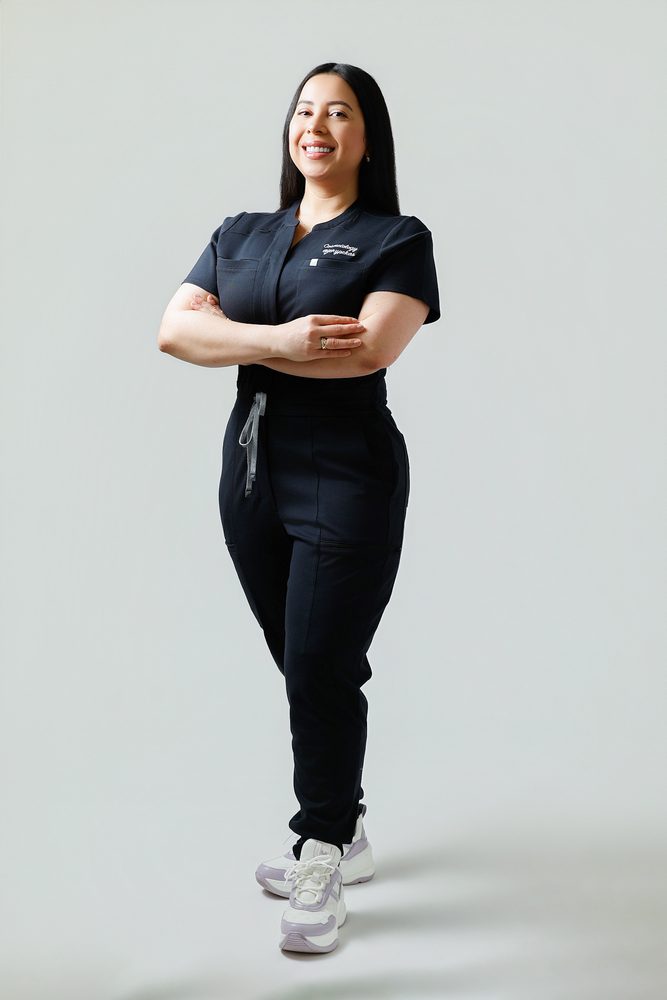 Confident full-length pose of a woman in black scrubs facing the camera with arms folded and one foot forward