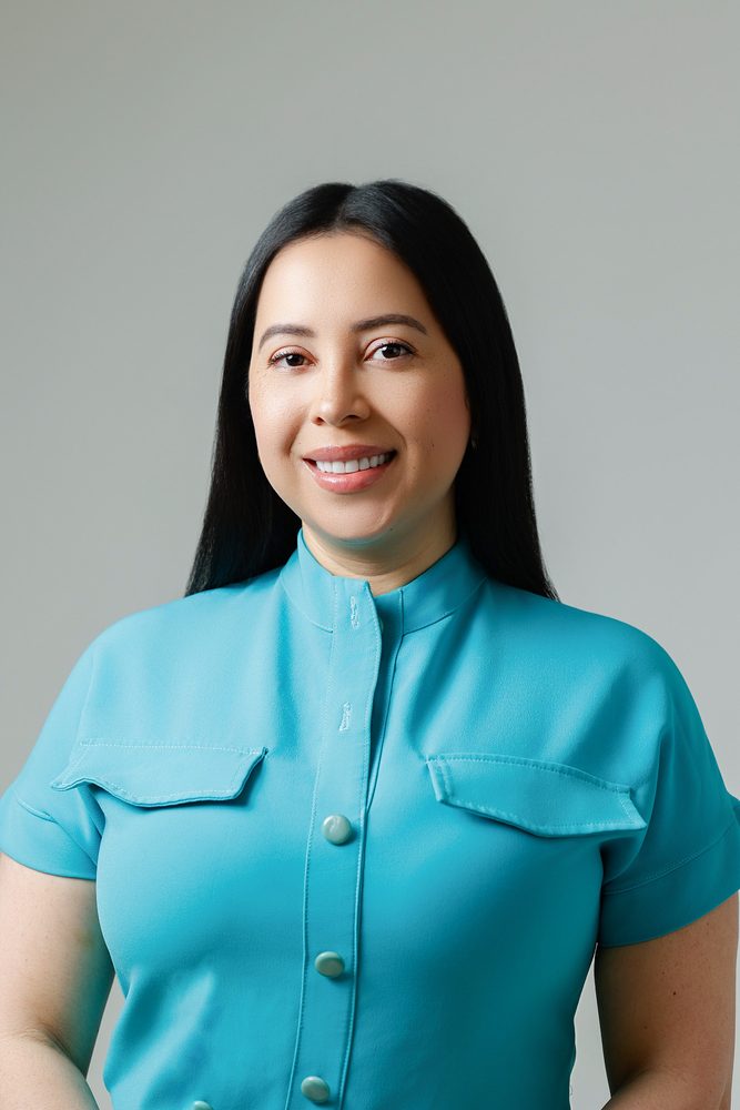 Headshot of a smiling woman with long dark hair in a teal button-front uniform on a gray backdrop