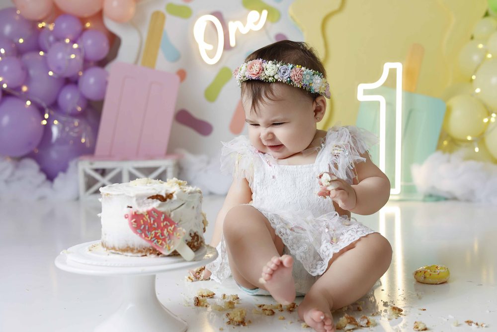 Baby scrunching her face with a fistful of cake, crumbs scattered around a popsicle-decorated cake