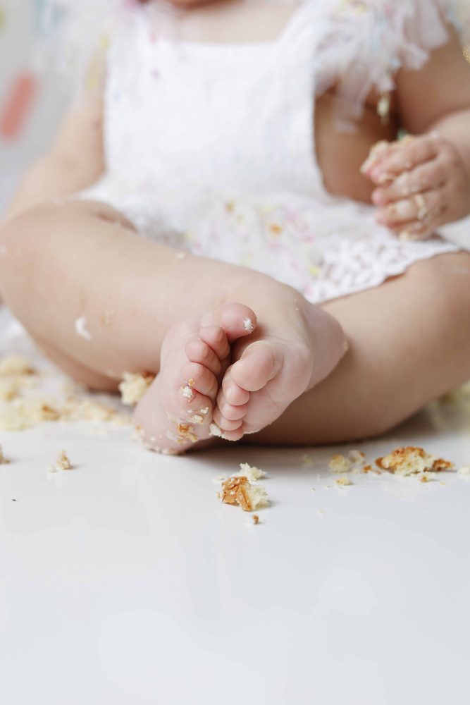 Close-up of a baby's crumb-covered bare feet and frosting-sticky hands after the cake smash