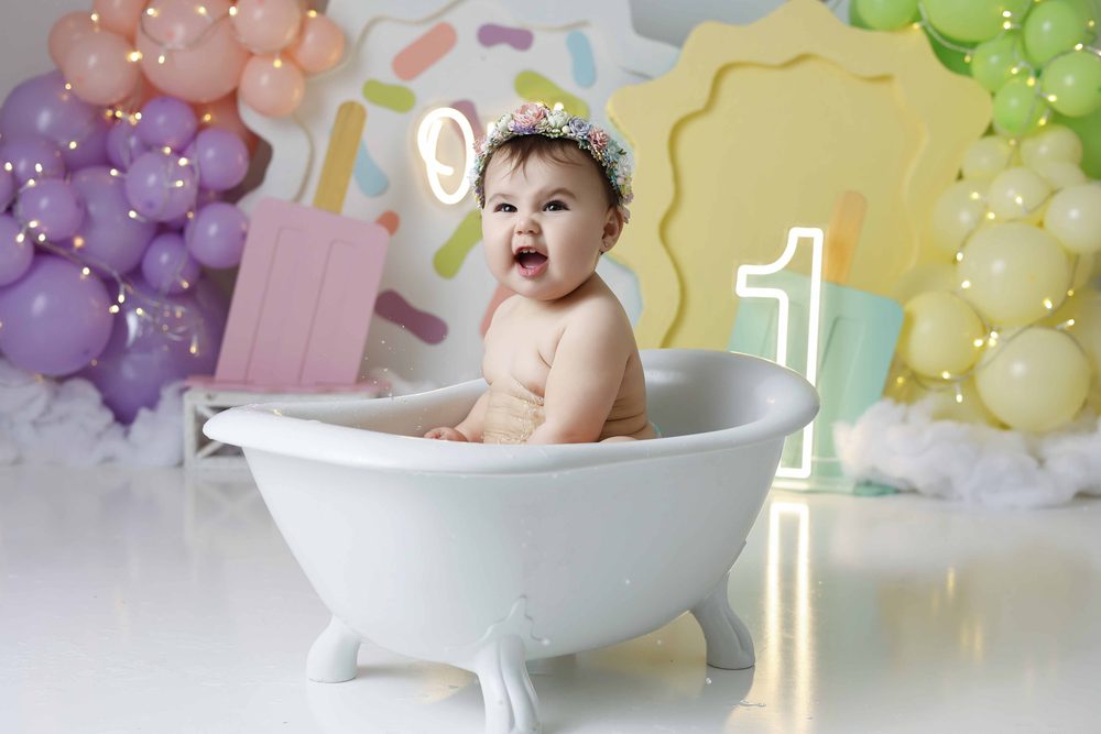 Laughing baby in a flower crown sitting in a white clawfoot tub for a post-smash splash