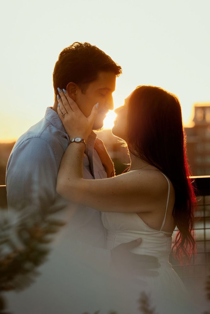 Couple about to kiss as the setting sun glows between their faces, her blue-painted nails on his cheek