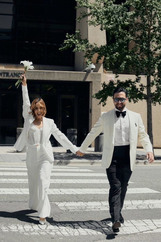 Bride raises her calla lily bouquet in celebration as the newlyweds cross a downtown crosswalk hand in hand