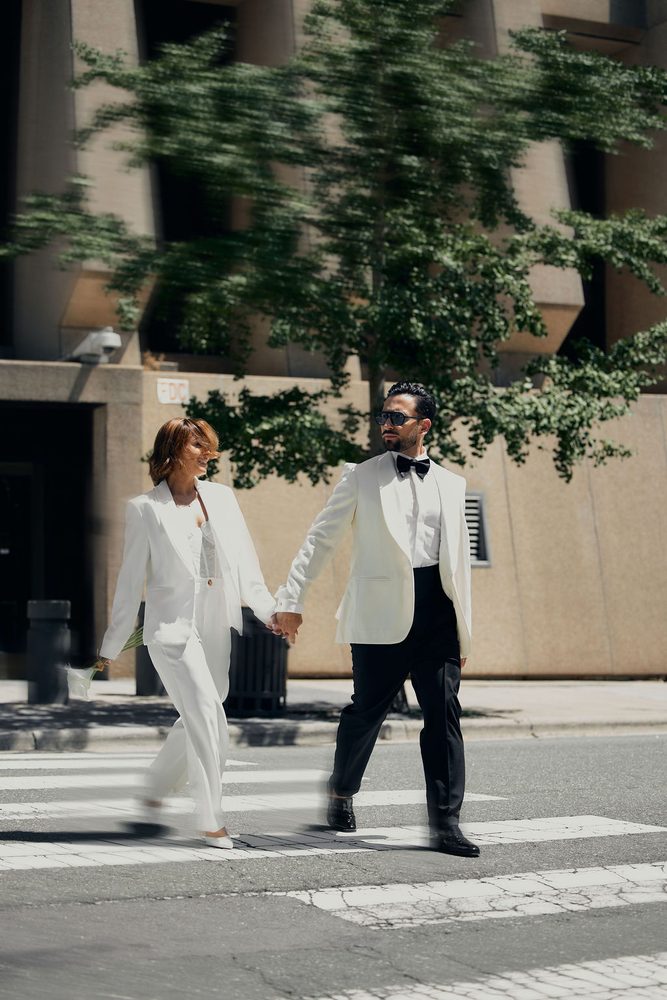 Bride and groom striding across the street after their ceremony, trees blurred with motion behind them
