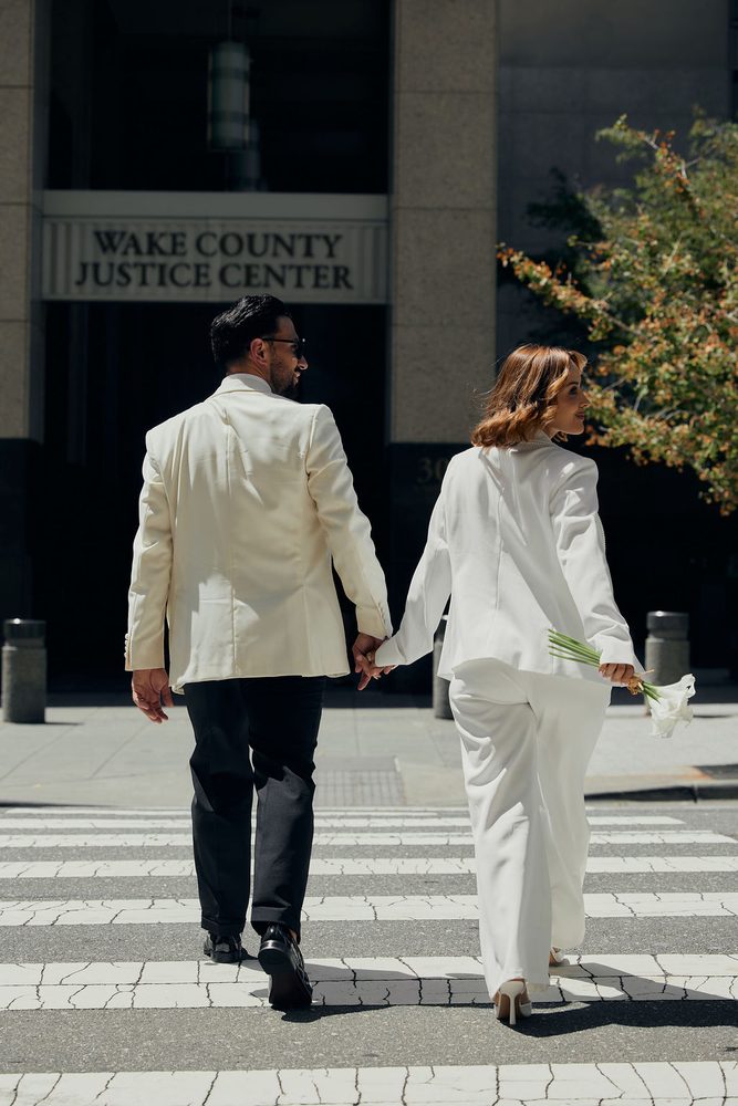 Bride glances back over her shoulder, calla lilies in hand, as the couple walks toward the justice center