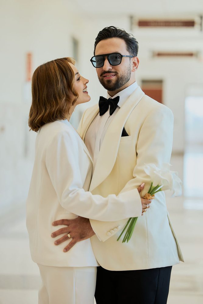 Close embrace in a bright courthouse hallway, the bride laughing up at her groom as his hand rests at her waist