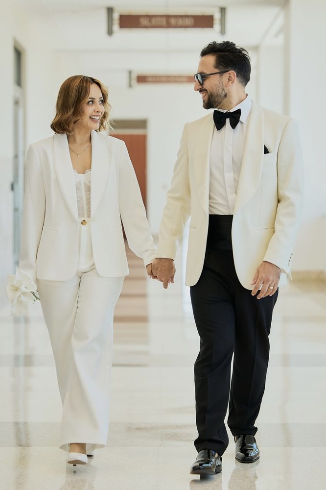 Newlyweds walking hand in hand down a polished marble courthouse hallway, smiling at each other