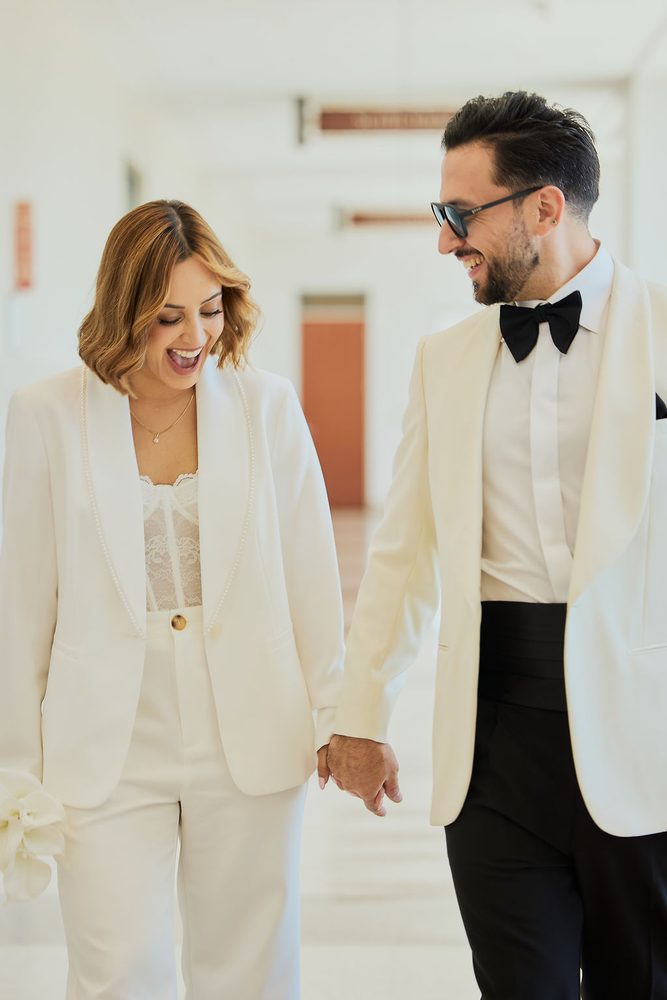 Bride laughing and looking down as she holds her groom's hand in a sunlit courthouse corridor
