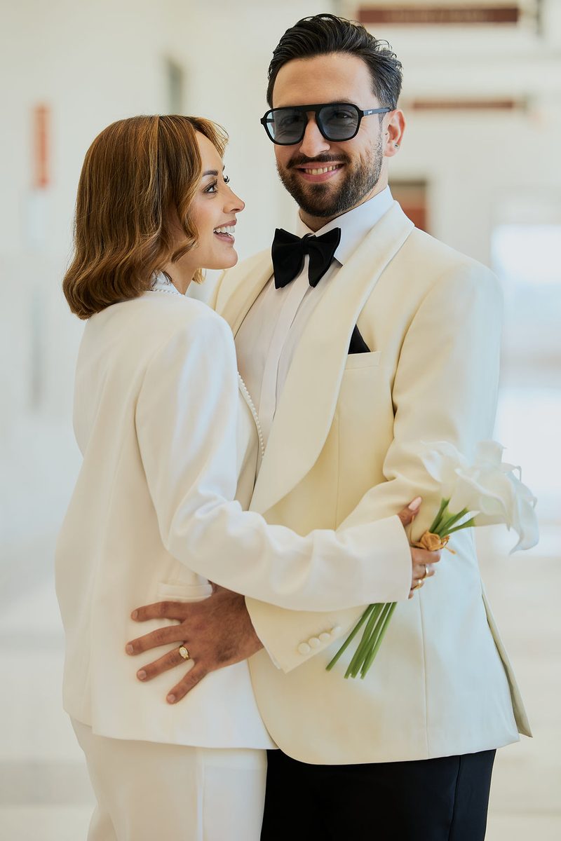 Courthouse wedding photography: bride in a white pantsuit embracing her groom in an ivory tuxedo jacket