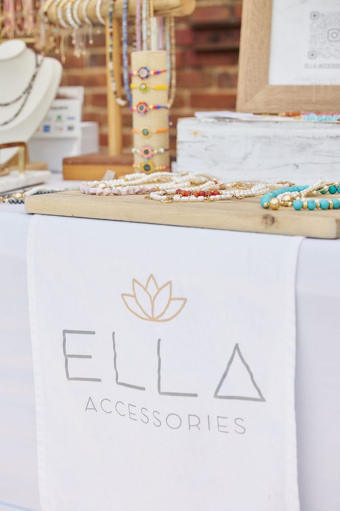 Beaded bracelets and necklaces on wooden displays at a jewelry vendor table with a lotus-logo table runner