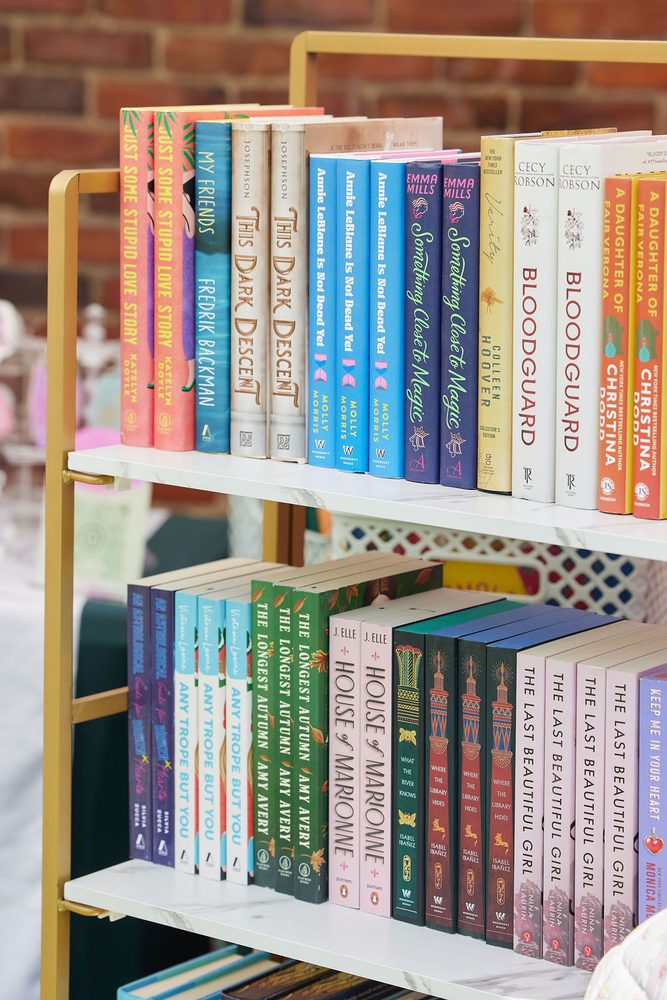 Colorful rows of novels on a gold shelving unit at a pop-up book vendor booth against a brick wall