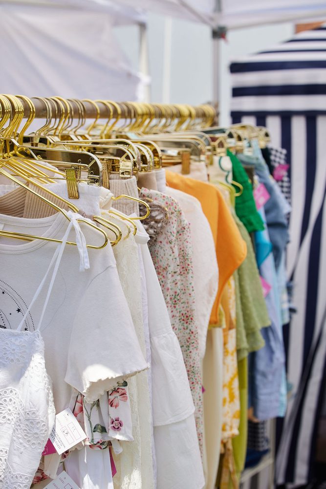 Rack of white, floral and pastel women's clothing on gold hangers under a striped vendor tent