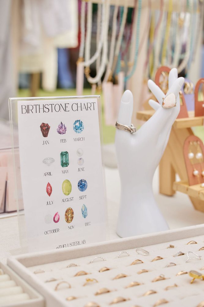 Birthstone chart sign, rings on a white hand display and a tray of gold rings at a jewelry booth