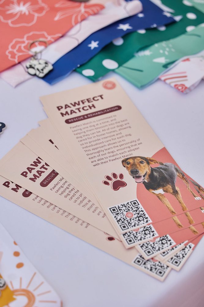 Dog rescue flyers with QR codes fanned out beside colorful pet bandanas on a vendor table