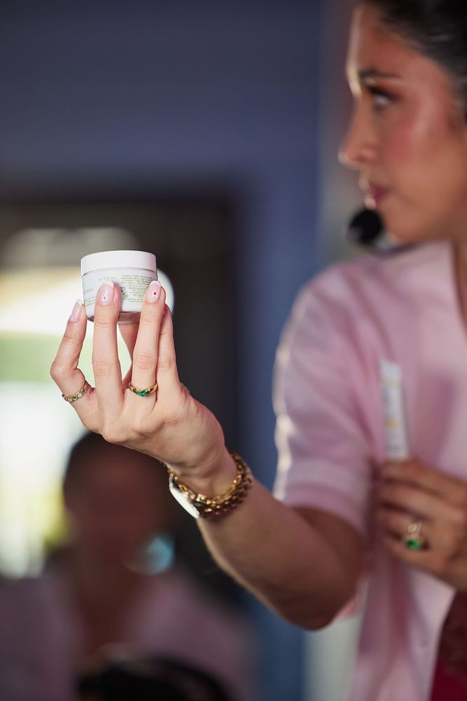 Woman wearing gold rings and bracelets holding up a jar of face cream during a beauty presentation