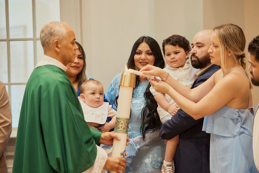 Family holding a baby and lighting a small candle from the tall ceremonial candle held by the officiant