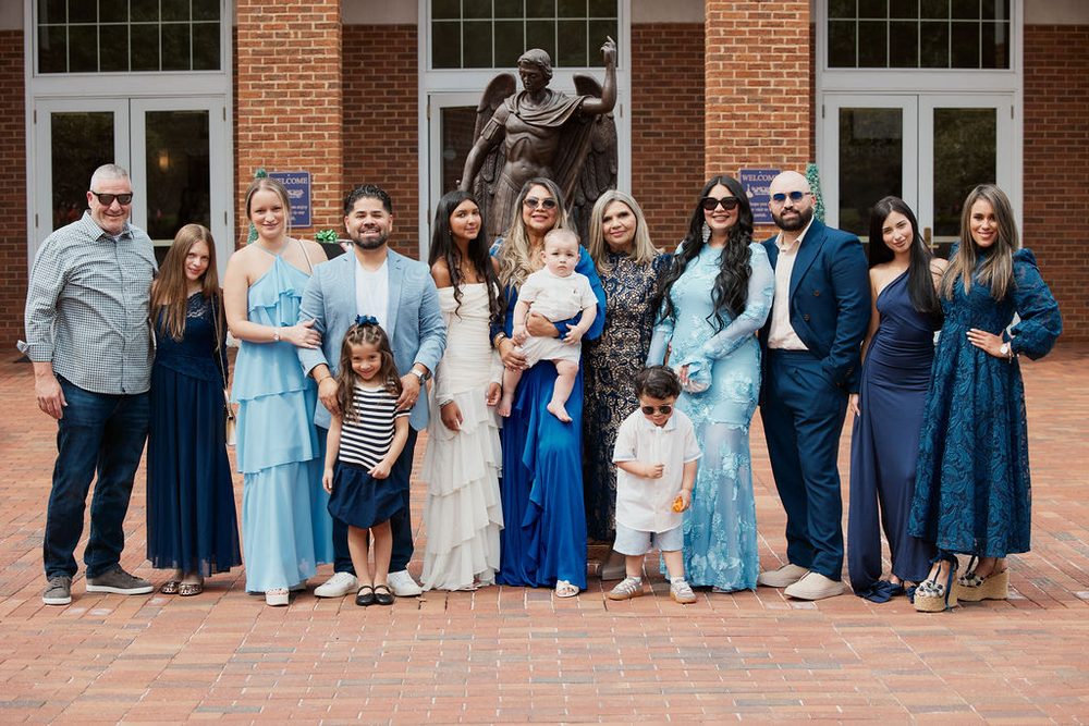 Large family in blue and navy outfits posing with a baby in front of a brick building and bronze statue