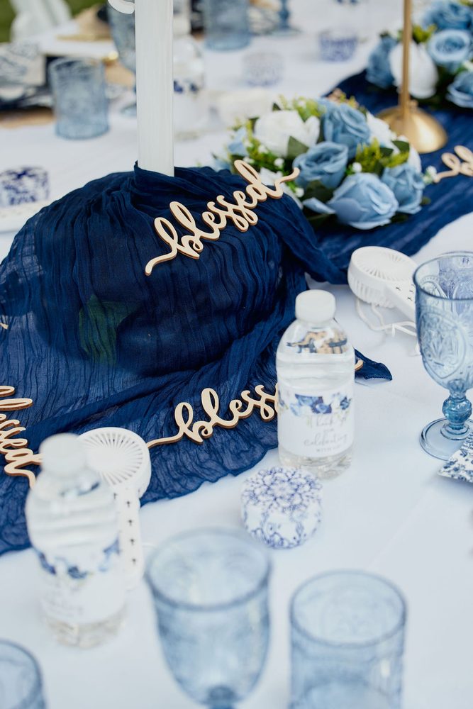 Navy table runner with gold script 'blessed' cutouts, blue roses and personalized water bottles