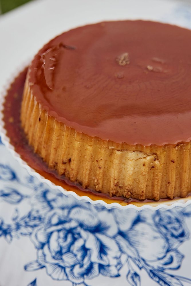 Close-up of a caramel-glazed flan on a scalloped white plate over a blue floral tablecloth