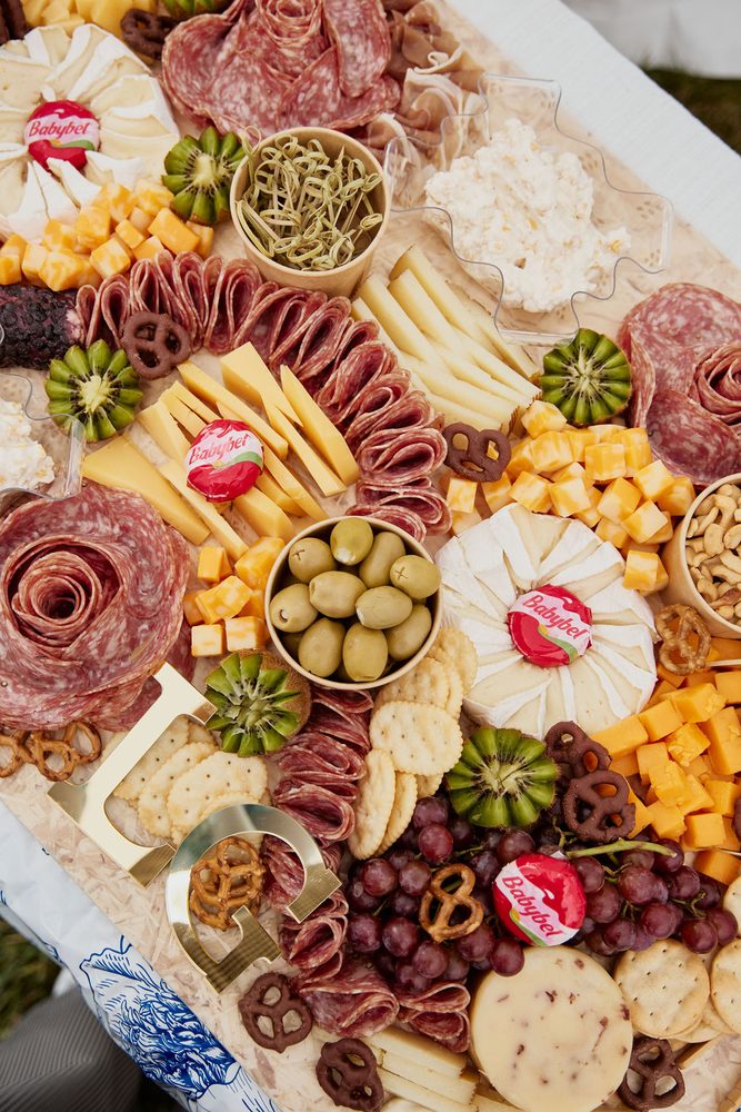 Overhead view of a large grazing table with salami roses, brie, cheddar cubes, olives, kiwi and grapes
