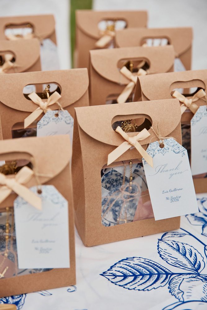 Rows of kraft paper favor bags with cream ribbons and blue 'Thank you' tags on a floral tablecloth