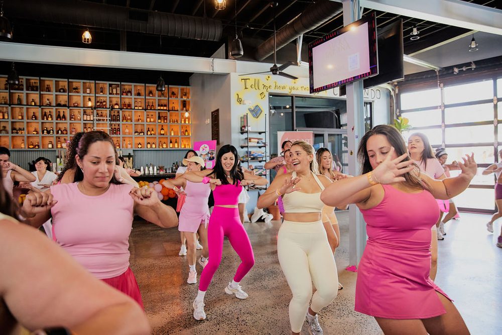 Women in pink activewear dancing together during a group dance fitness class at a studio launch