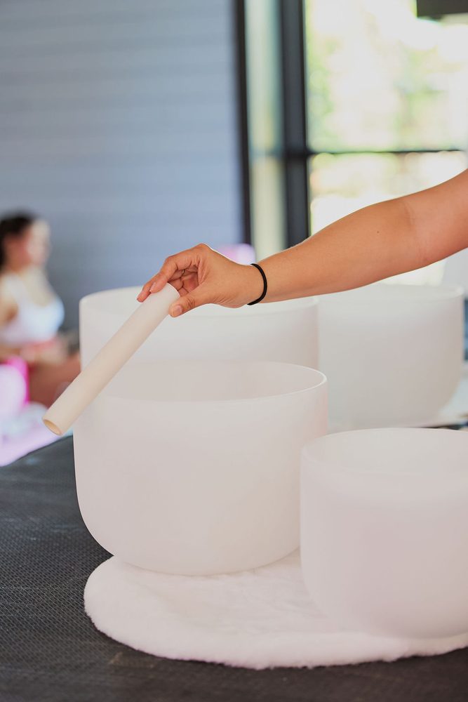 Hand circling a mallet around the rim of a frosted crystal singing bowl set on a white fur mat