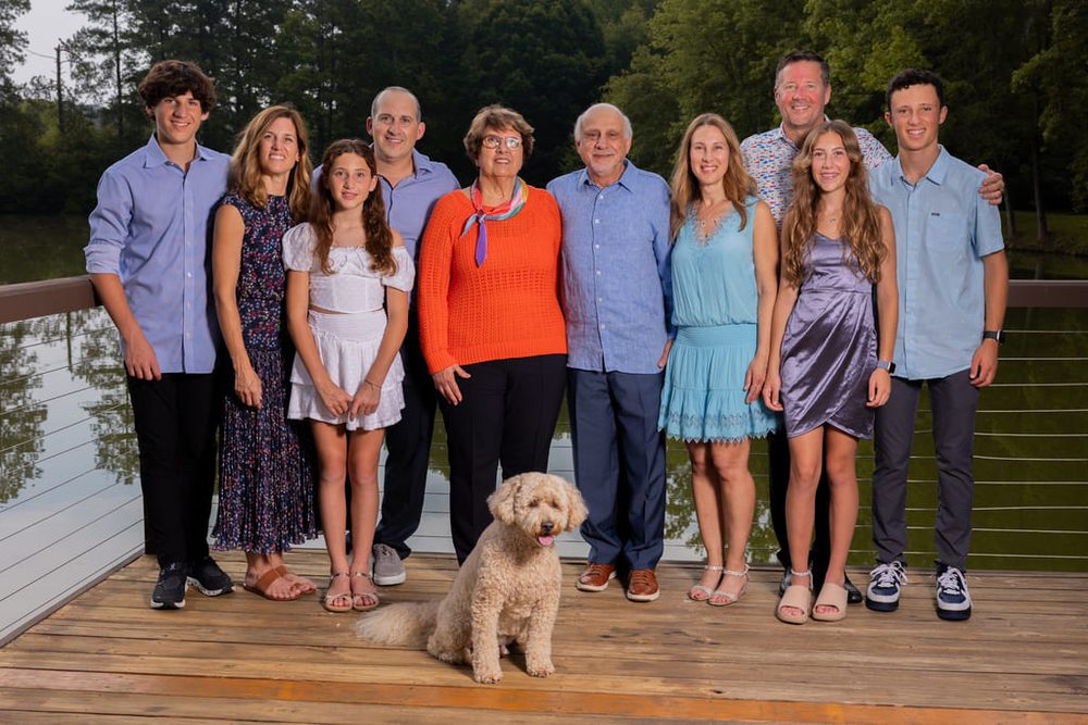 Multigenerational family of ten and a curly-haired dog posing on a lakeside wooden deck