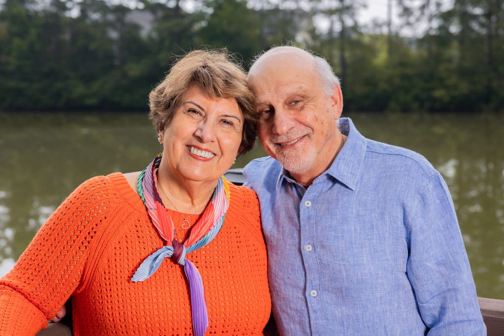 Close-up of a smiling grandmother in an orange sweater and grandfather leaning together by a lake