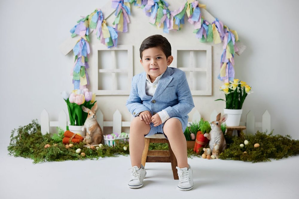 Little boy in a light blue blazer on a wooden stool in an Easter set with bunnies, tulips and ribbon garland