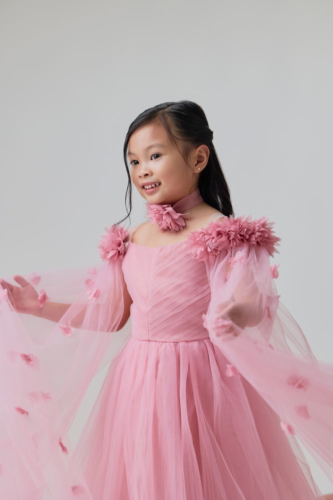 Smiling girl in a pink tulle gown with floral shoulders, swirling her sheer petal-trimmed cape