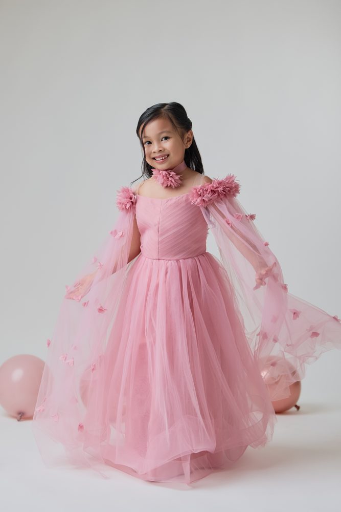 Girl in a pink tulle princess dress smiling with her cape spread out, pink balloons on the floor behind