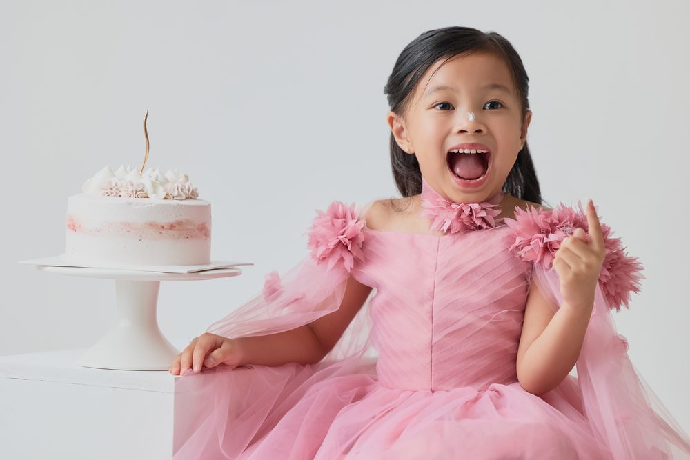 Girl with a dab of frosting on her nose, mouth open in delight, next to a cake with a gold candle