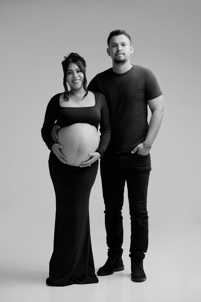 Black-and-white full-length portrait of expectant parents standing side by side in matching black outfits