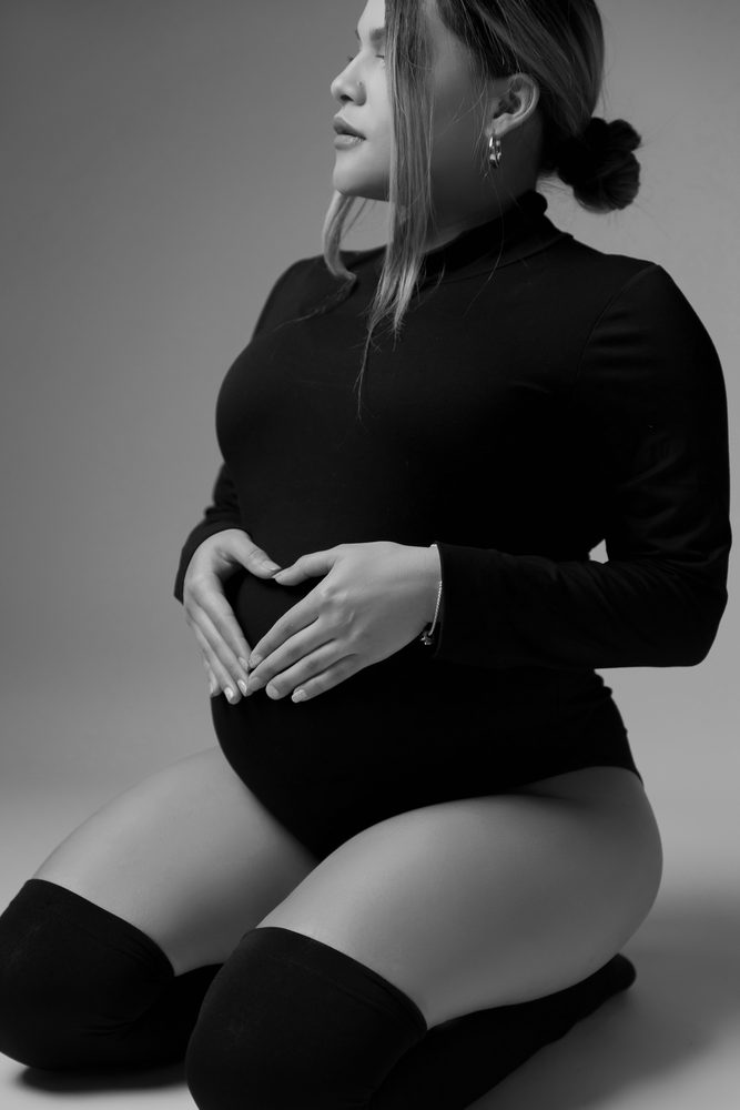 Close black-and-white shot of an expectant mother forming a heart with her hands over her belly