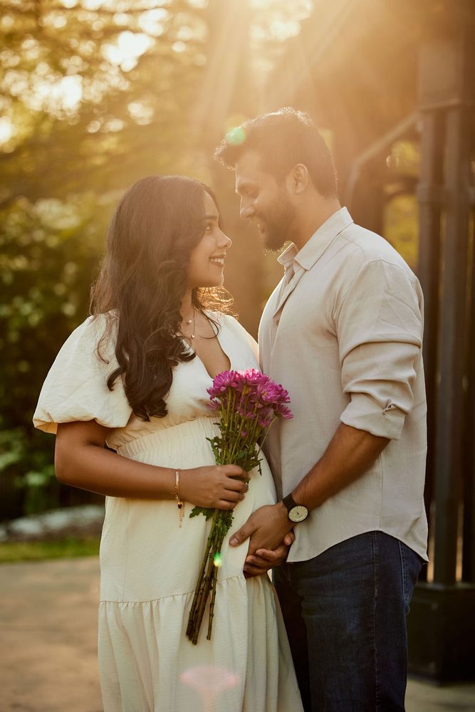Expectant couple gazing at each other in golden backlight as she holds a bunch of pink chrysanthemums