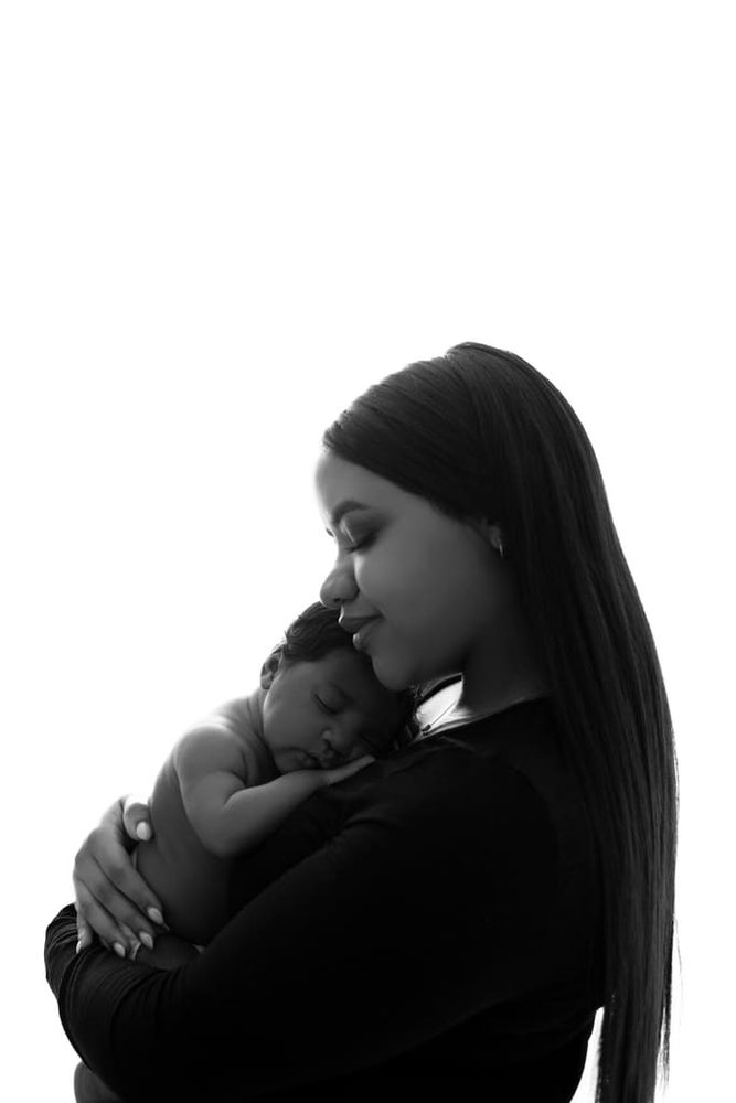 Black-and-white silhouette of a mother cheek to cheek with her sleeping newborn held against her shoulder