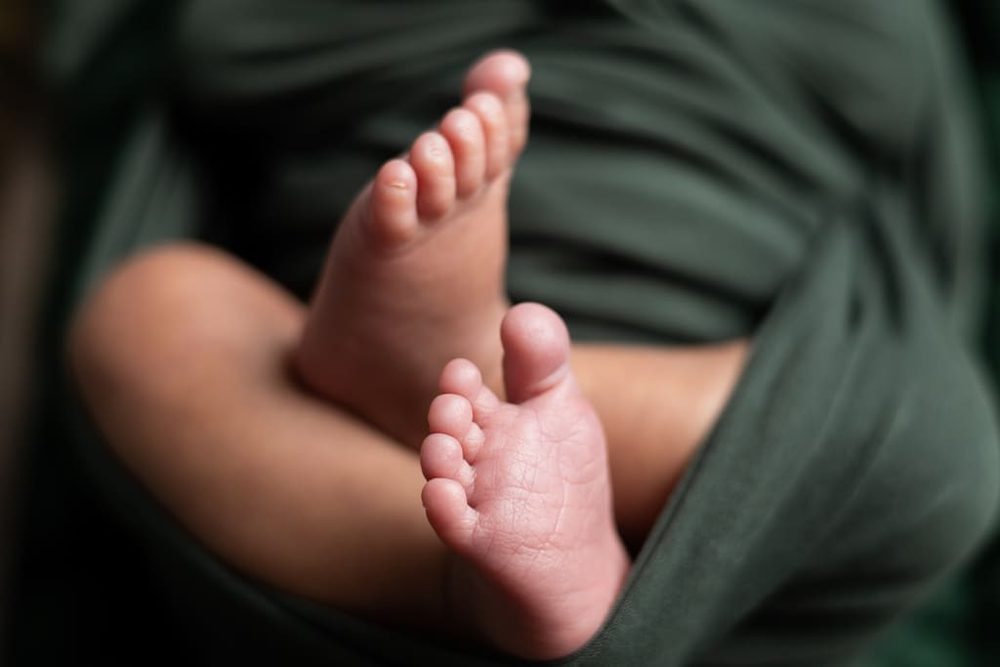 Close-up of a newborn's tiny crossed feet peeking out of a dark green wrap