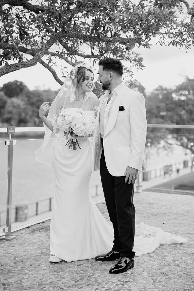 Black-and-white shot of the bride lifting her veil and smiling as the groom looks down at her