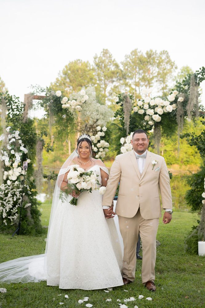 Smiling newlyweds walking hand in hand away from the floral arch as soap bubbles float around them