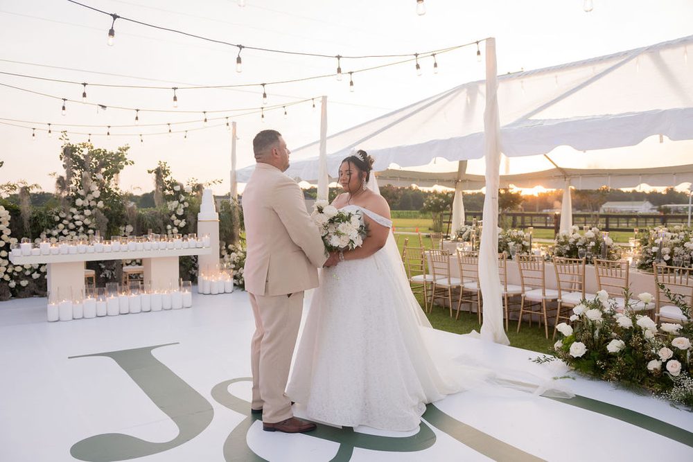 Bride and groom sharing a quiet moment on a monogrammed white dance floor under string lights by the reception tent