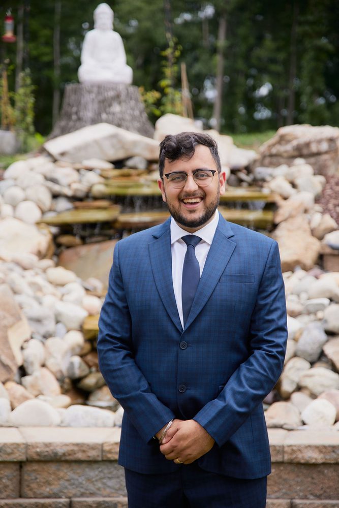 Smiling groom in a navy plaid suit and glasses standing before a rock garden waterfall