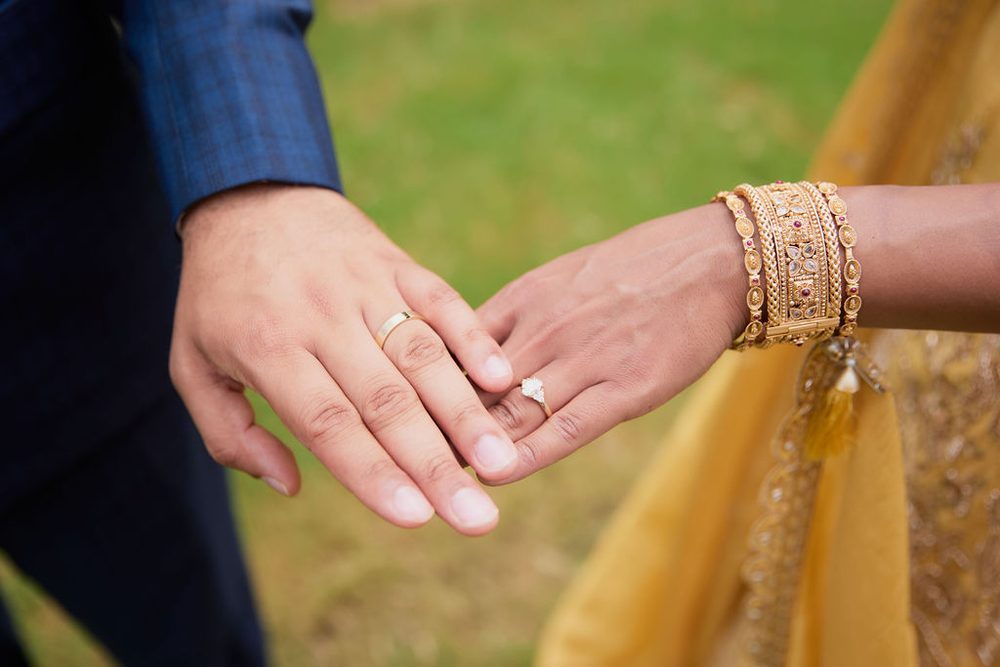 Close-up of the couple's hands showing a gold band, diamond engagement ring and ornate gold bangles